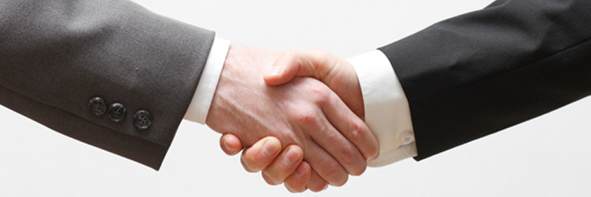 two suited people's arms shaking hands