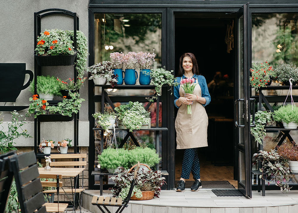 Stock image of a plant shop front with a lady standing in the doorway holding a bunch of pink tulips